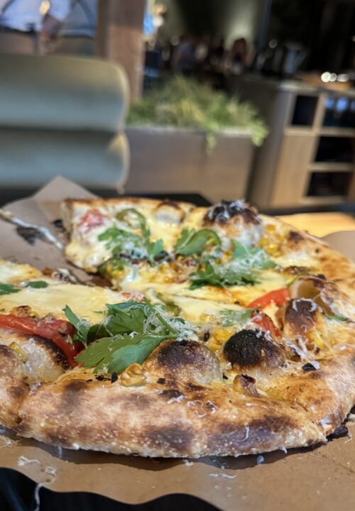 A thin, crisp wood-fired pizza topped with seasonal ingredients, balancing smoky crust, creamy cheese, and bright Mediterranean flavors.